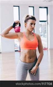 Young fitnesswoman holding and training with a kettle. Fit lifestyle. Gym equipment.. Young fitnesswoman training with a kettle