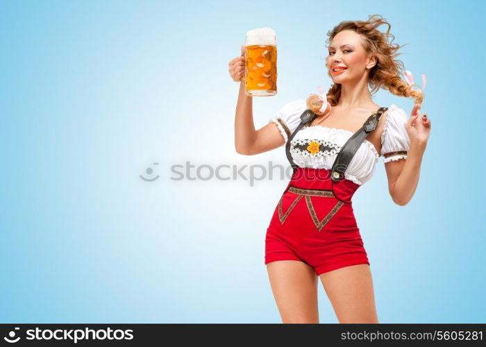 Young flirting sexy Swiss woman wearing red jumper shorts with suspenders in a form of a traditional dirndl, holding a beer mug on blue background.