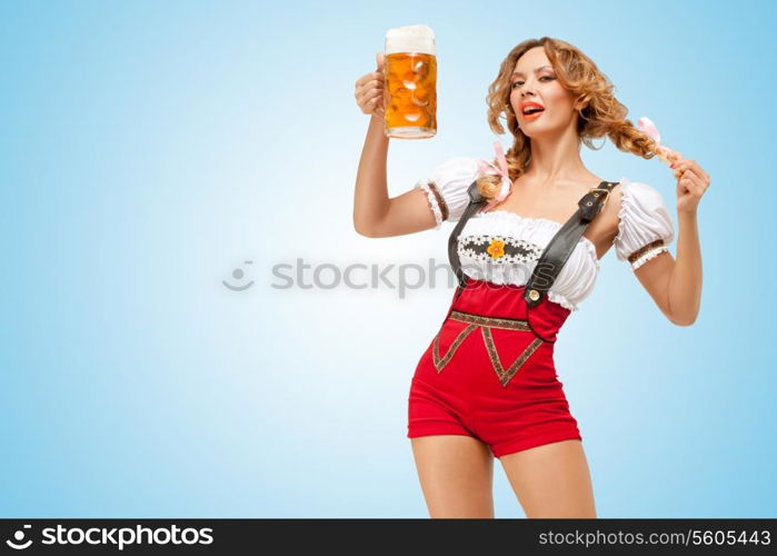 Young flirting sexy Swiss woman wearing red jumper shorts with suspenders in a form of a traditional dirndl, holding a beer mug on blue background.