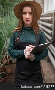 Young florist in hat with clipboard in botanical garden.. Florist in botanical garden.