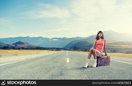 Young free hitchhiker. Traveler woman sits on retro suitcase and waiting for car