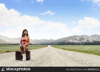 Young free hitchhiker. Traveler woman sits on retro suitcase and waiting for car