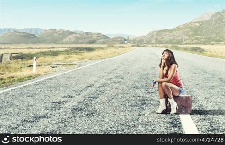 Young free hitchhiker. Traveler woman sits on retro suitcase and waiting for car