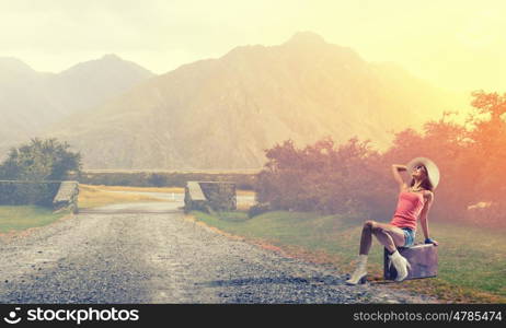 Young free hitchhiker. Traveler woman sits on retro suitcase and waiting for car