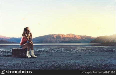 Young free hitchhiker. Traveler woman sits on retro suitcase and waiting for car