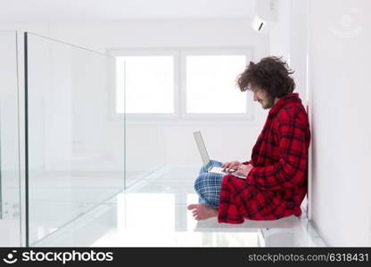 young freelancer in bathrobe working from home using laptop computer while sitting on floor