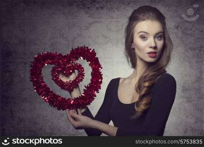 Young, fresh, romantic, pretty valentine girl with nice hairstyle and makeup is holding a heart.