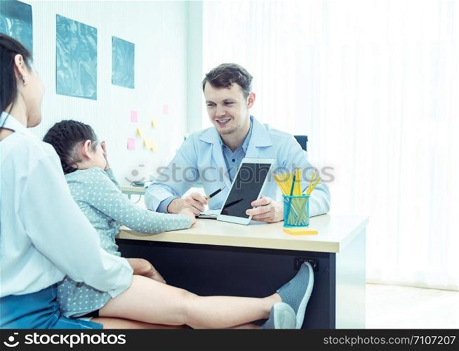 Young friendly caucasian pediatrician doctor is examining child patient girl with her mother ,consultation with a stethoscope and tablet pc in clinic office .Healthcare and medical kid concept