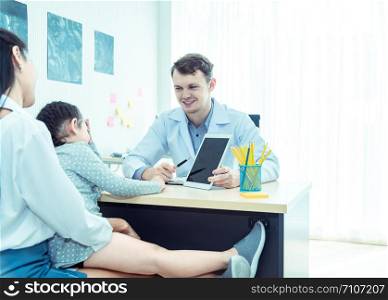 Young friendly caucasian pediatrician doctor is examining child patient girl with her mother ,consultation with a stethoscope and tablet pc in clinic office .Healthcare and medical kid concept