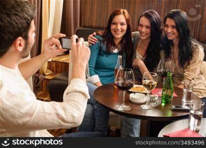 Young friends at the bar man take picture of three women