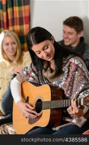 Young friends in winter cottage play guitar spend holiday break
