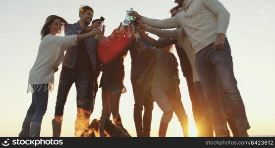 Young Friends Making A Toast With Beer and having fun Around Campfire at beach party on autumn day