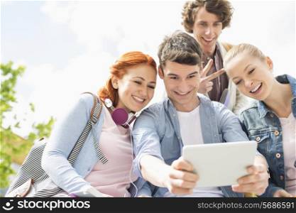 Young friends photographing themselves through digital tablet at college campus