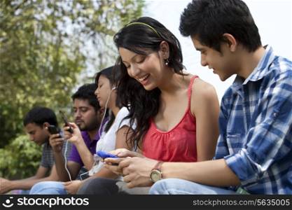 Young friends using cell phone with people in the background