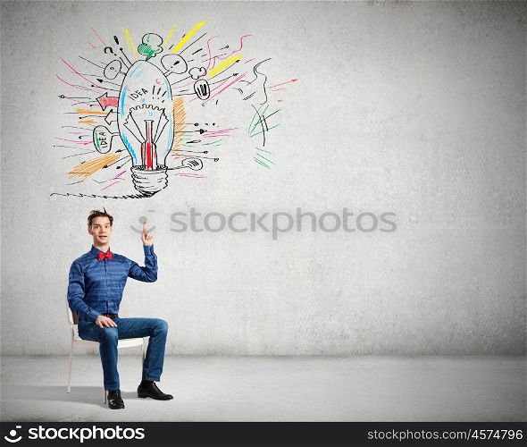 Young funny guy sitting in chair and pointing upwards