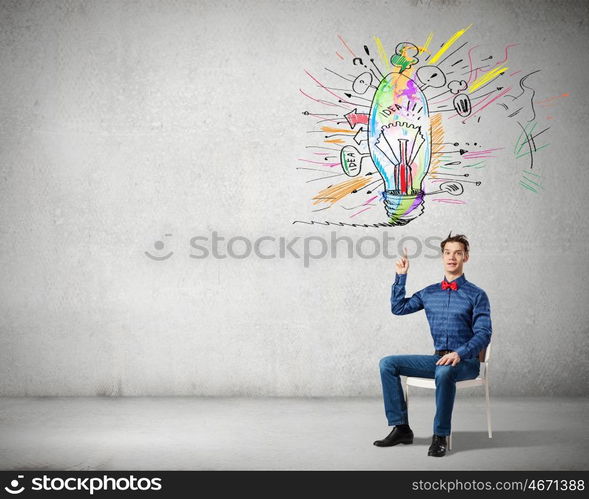 Young funny guy sitting in chair and pointing upwards