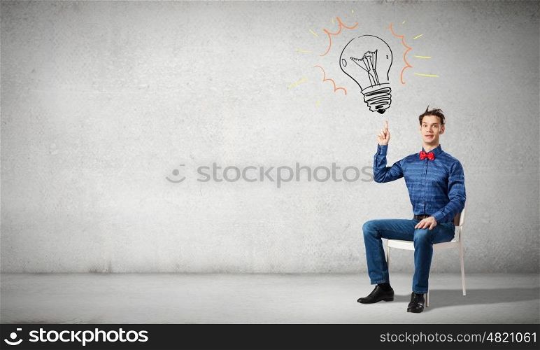 Young funny guy sitting in chair and pointing upwards