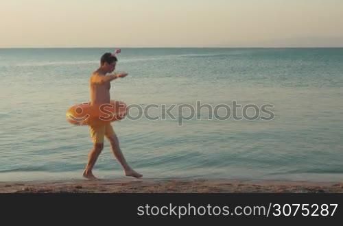 Young funny man with rubber ring performing humorous ballet dancing on the beach