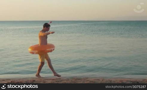 Young funny man with rubber ring performing humorous ballet dancing on the beach