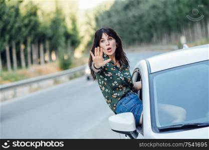 Young funny woman peeking her body through the window of the car in a beautiful poplar field. Lifestyle concept.. Woman peeking her body through the window of the car