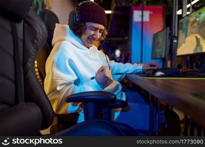 Young gamer in headphones play in game club. Virtual entertainment, e-sport tournament, cybersport lifestyle. Male person leisures in internet cafe. Young gamer in headphones play in game club