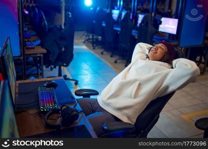 Young gamer resting in gaming armchair, game club. Virtual entertainment, e-sport tournament, cybersport lifestyle. Male person leisures in internet cafe. Young gamer resting in gaming armchair, game club