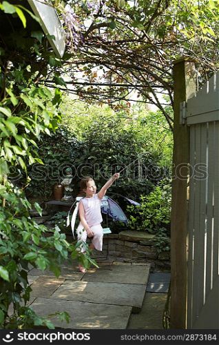 Young girl (5-6) sitting in garden in fairy costume holding magic wand