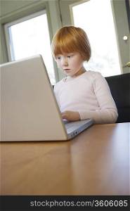 Young girl (5-6) using laptop, concentrated
