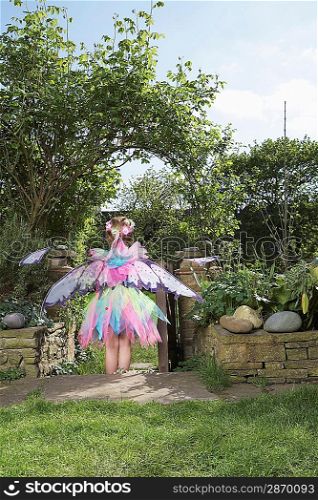 Young girl (5-6) wearing fairy costume standing in garden back view