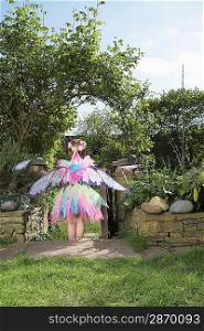 Young girl (5-6) wearing fairy costume standing in garden back view