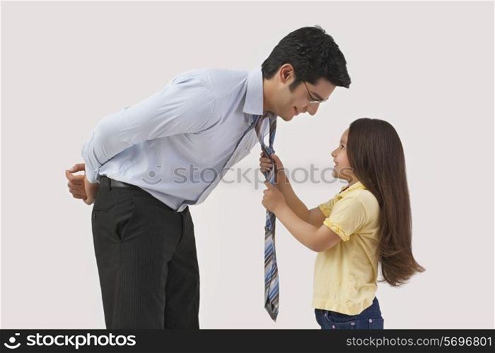Young girl adjusting father&rsquo;s tie over colored background
