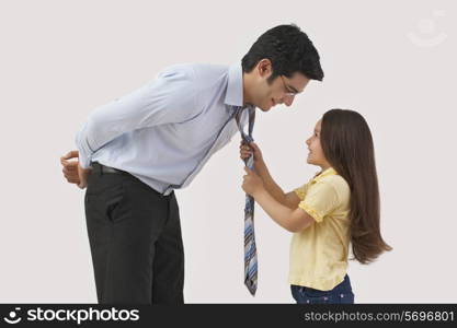 Young girl adjusting father&rsquo;s tie over colored background