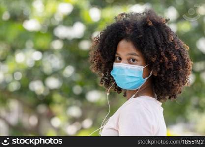 Young girl afro in face mask going at reopen school after covid-19 quarantine and lockdown. It is new normal for protection and prevention while outbreak of coronavirus or flu. back to school concept.