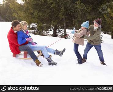 Young Girl And Boy Pulling Parents Through Snow On Sled
