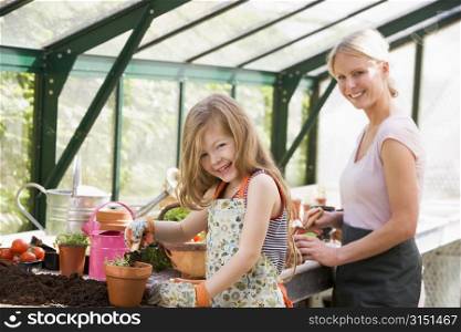 Young girl and woman in greenhouse putting soil in pots smiling