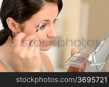 Young girl applying eyeshadow on eyelid looking at mirror