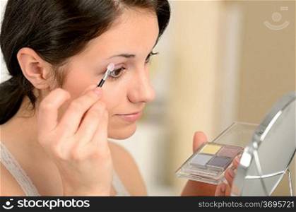 Young girl applying eyeshadow on eyelid looking at mirror