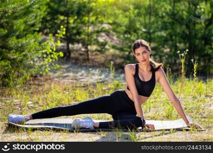 Young girl athlete sits on the mat for training in the forest. Young beautiful girl athlete sits on mat in forest