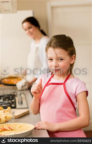 Young girl baking apple pie thumb up tasting with mother