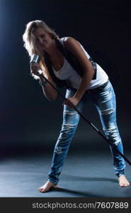 young, girl, blonde, jeans, clothes on a dark background emotionally sings into a microphone