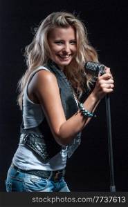 young, girl, blonde, jeans, clothes on a dark background emotionally sings into a microphone