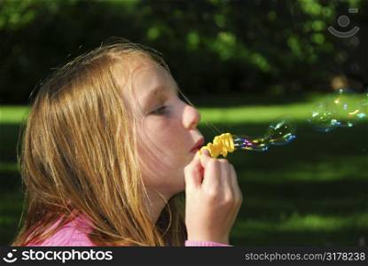 Young girl blowing soap bubbles in a park