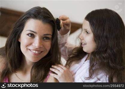 Young girl brushing woman&acute;s hair on bed in bedroom smiling (selective focus)