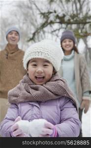 Young girl carrying snow balls in front of parents in park in winter