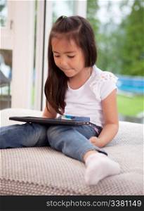 Young girl child looking at a digital tablet sitting on a couch cushion