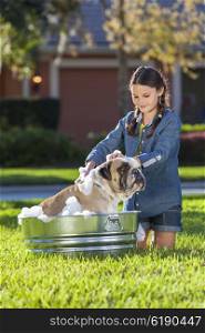 Young girl child washing her pet dog, a bulldog, outside in a metal tub