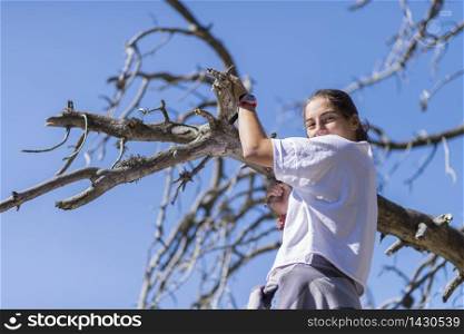 Young girl climbing a tree while looking at the camera