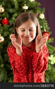Young Girl Crossing Fingers In Front Of Christmas Tree