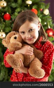 Young Girl Cuddling Teddy Bear In Front Of Christmas Tree