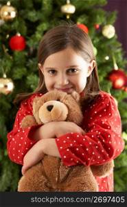 Young Girl Cuddling Teddy Bear In Front Of Christmas Tree